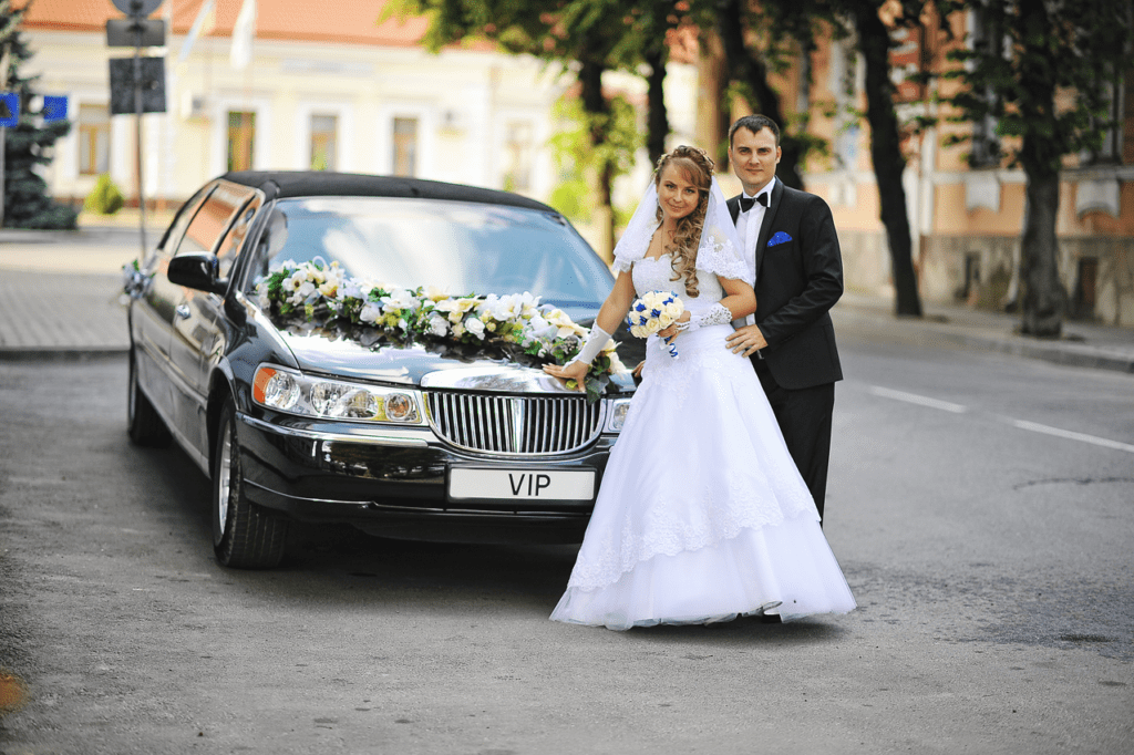 The cost and budget considerations for a wedding limo or car services in NYC 8 Bride and groom posing beside a decorated black limousine with VIP plate, symbolizing elegant wedding limo service.
