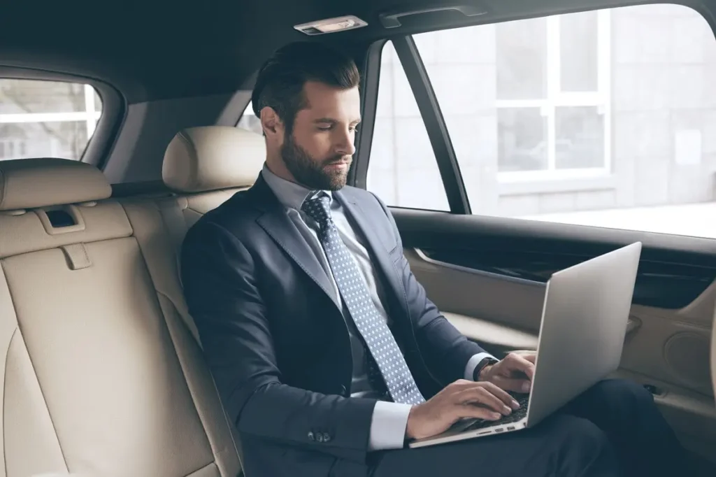 Businessman in a suit working on his laptop inside a luxury limousine, showcasing comfort and efficiency during corporate travel.