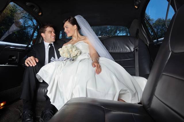 Bride and groom standing beside a beautifully decorated VIP limousine, ready for their wedding journey in style.