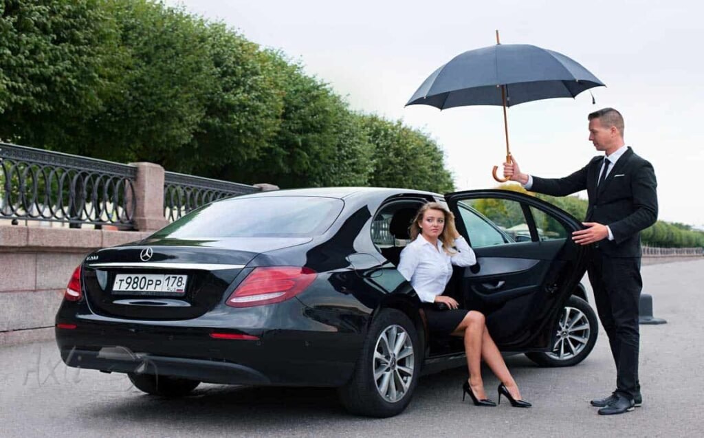 15 Etiquette and Expectations in Using a Limo or Chauffeur Service in New York City 15 Chauffeur holding umbrella for businesswoman exiting luxury black car, illustrating professional limo etiquette in NYC.