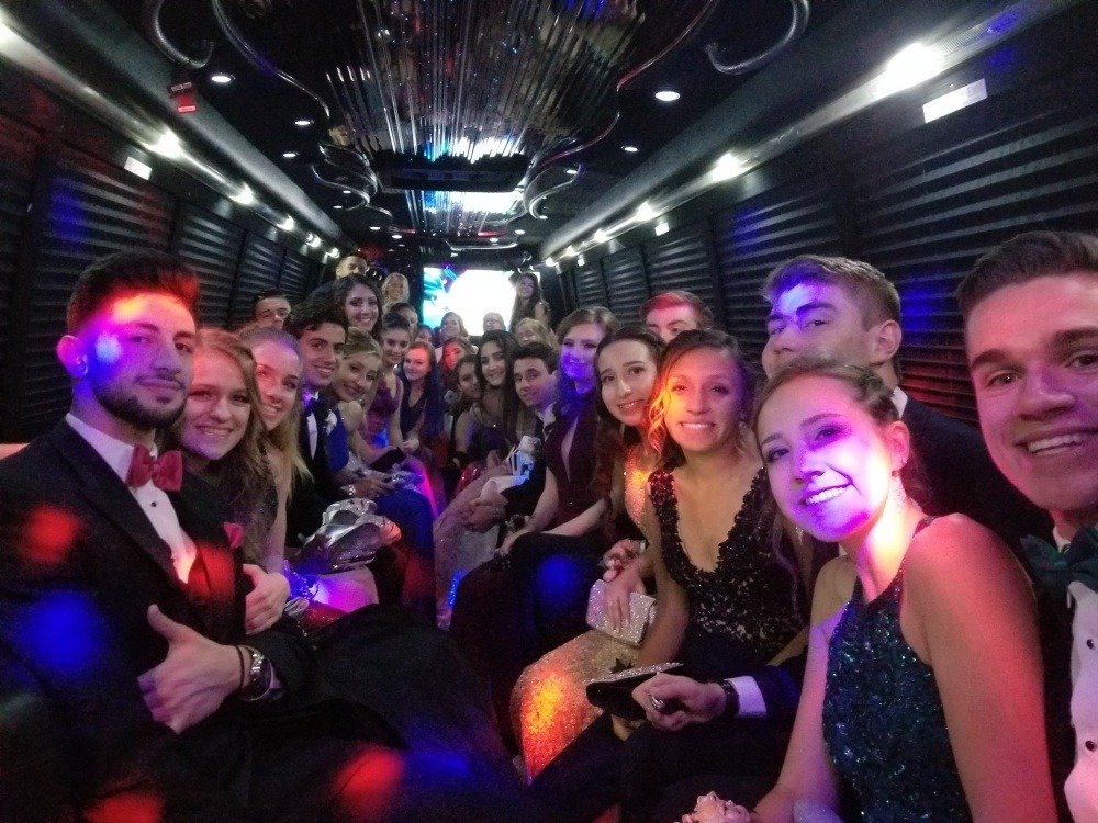 Planning for a Special Party Night in New York City? Rent a Limo for the Ultimate Experience 17 A group of young adults dressed in formal attire smile and pose for a photo inside a party bus with vibrant lighting and a festive atmosphere.