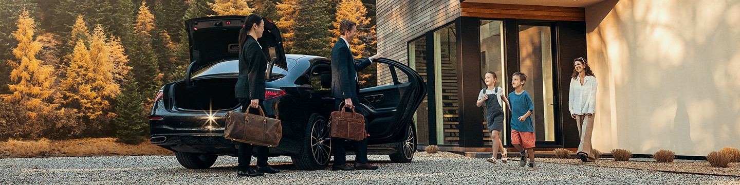 Family welcoming parents arriving in a luxury car outside a modern home surrounded by autumn trees and warm sunlight.