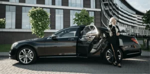 Elegant woman stepping out of a black luxury car, talking on the phone in front of a modern building