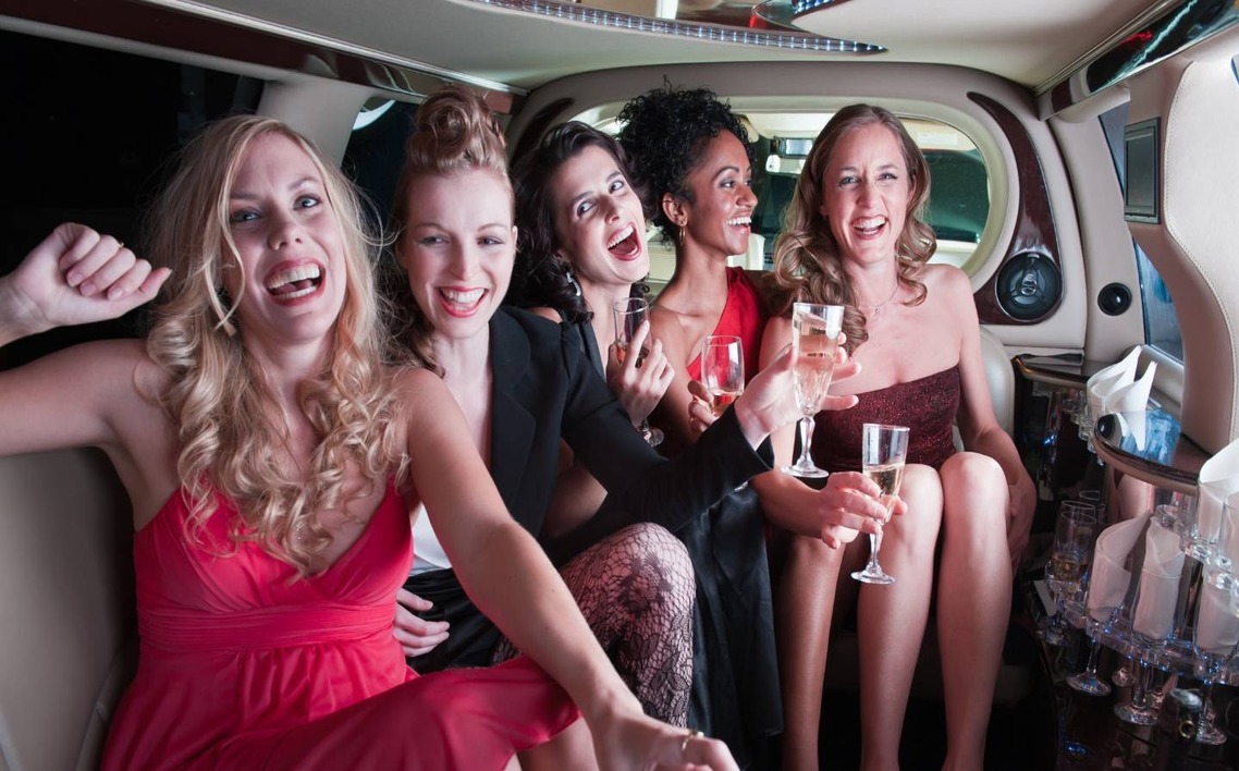 Group of women enjoying a glamorous prom night limo ride, celebrating with champagne and laughter in a luxury interior.