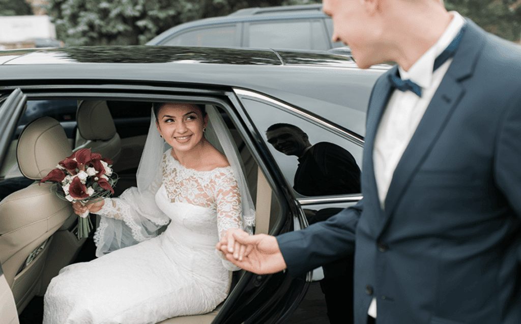 The cost and budget considerations for a wedding limo or car services in NYC 12 Bride stepping out of a luxury wedding limo, holding a bouquet, greeted by groom in NYC. Elegant wedding transport.