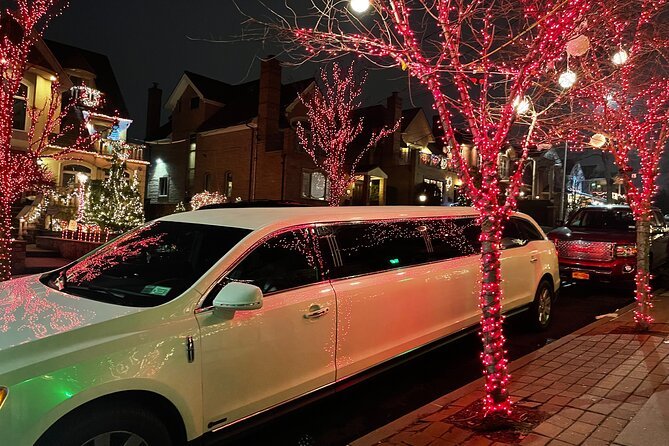 The Ultimate Guide to Christmas Light Limo Rides in NYC 2 A white limousine is parked on a festive residential street at night, surrounded by trees wrapped in glowing red holiday lights.