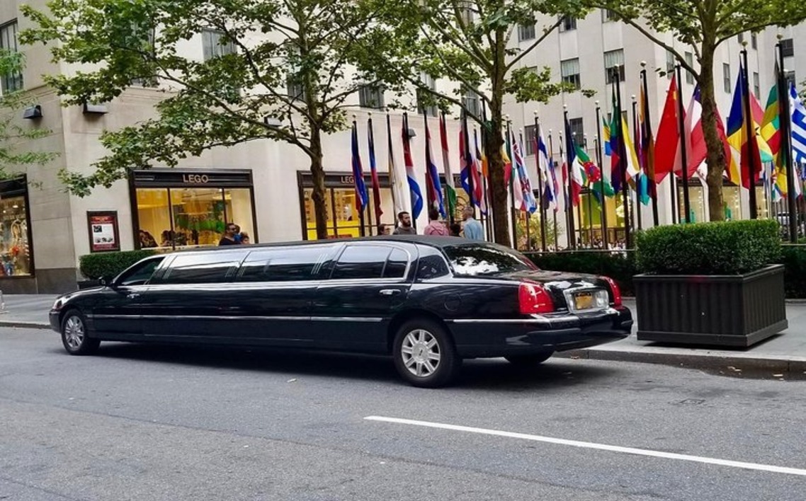 Black stretch limousine parked on a city street near the LEGO store and international flags at Rockefeller Center in New York City.