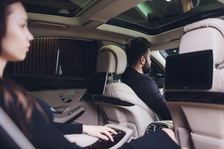 Executive businesswoman stepping out of a black luxury car, speaking on the phone in a corporate setting.