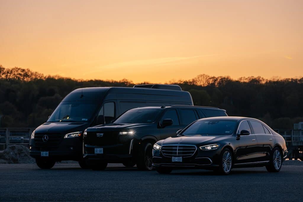 Luxury fleet of vehicles, including a Mercedes-Benz Sprinter van, Cadillac SUV, and Mercedes-Benz sedan, parked at sunset.