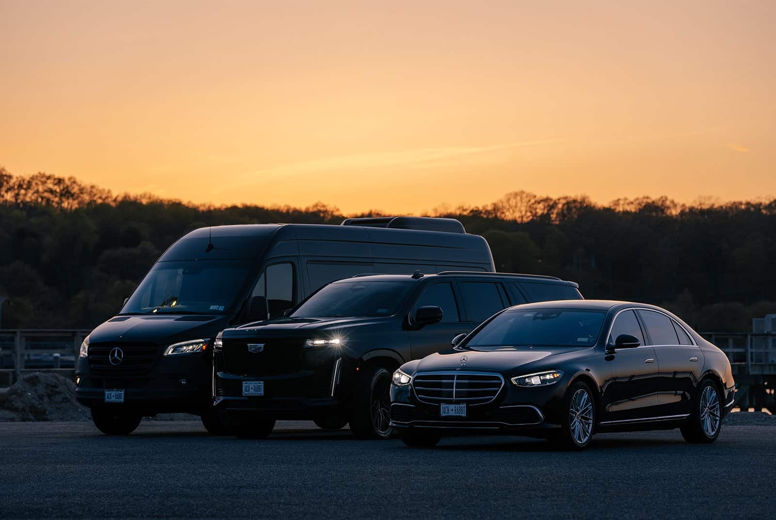 Luxury fleet of vehicles, including a Mercedes-Benz Sprinter van, Cadillac SUV, and Mercedes-Benz sedan, parked at sunset.