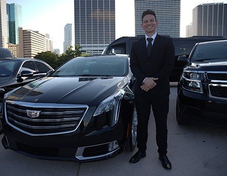 Professional chauffeur standing beside a luxury black Cadillac, ready for NYC hourly limo service, symbolizing premium transportation.