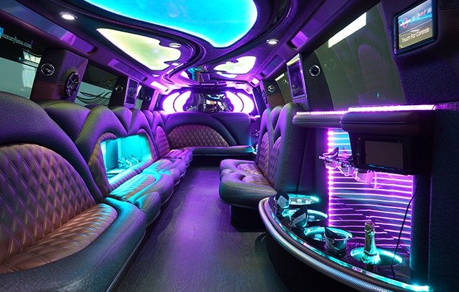Party Bus Rental NYC 3 Interior of a luxury party limousine with neon lighting, leather seating, TV screens, and a built-in bar with champagne glasses.
