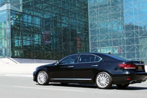 Black luxury car parked outside a glass airport terminal for group transportation service in New York City.