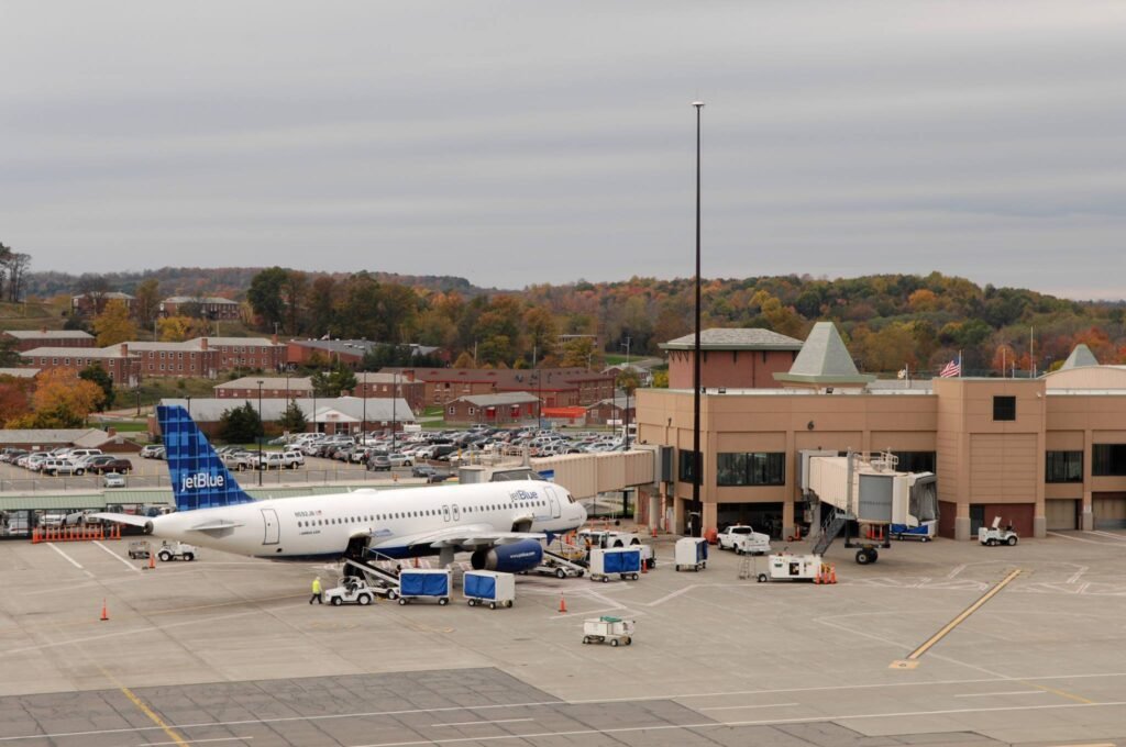 : JetBlue airplane at the gate of Stewart International Airport with terminal and autumn foliage in the background.