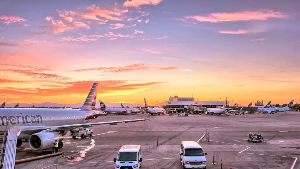 Commercial airplanes parked at an airport gate during a vibrant sunset with service vehicles nearby.