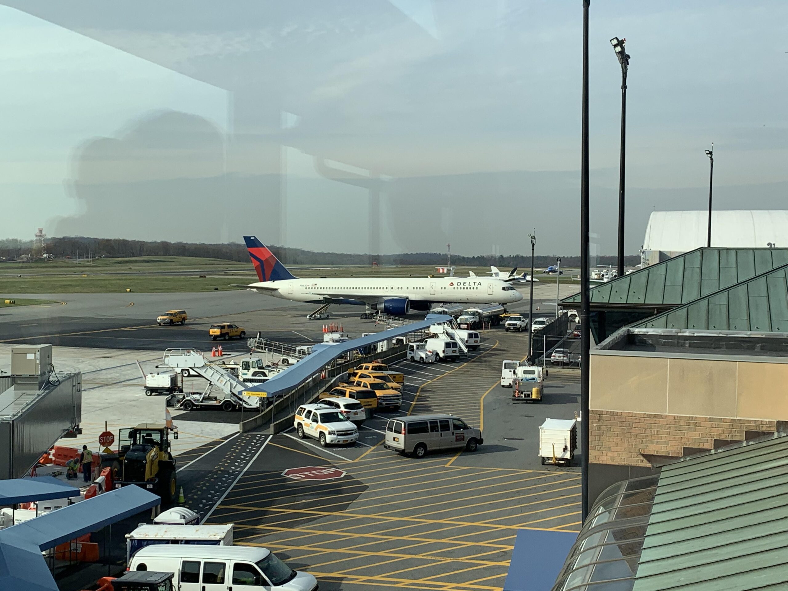 Delta Air Lines aircraft at the airport gate with surrounding service vehicles and terminal view.