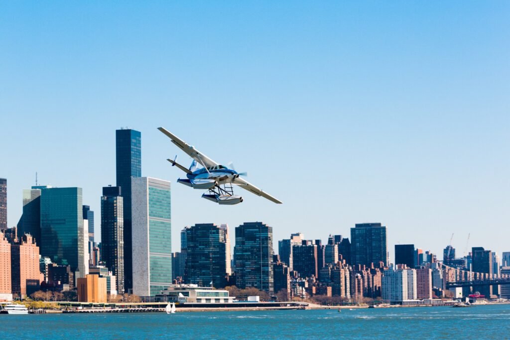 A seaplane takes off over the East River with the Manhattan skyline in the background on a clear day in New York City.