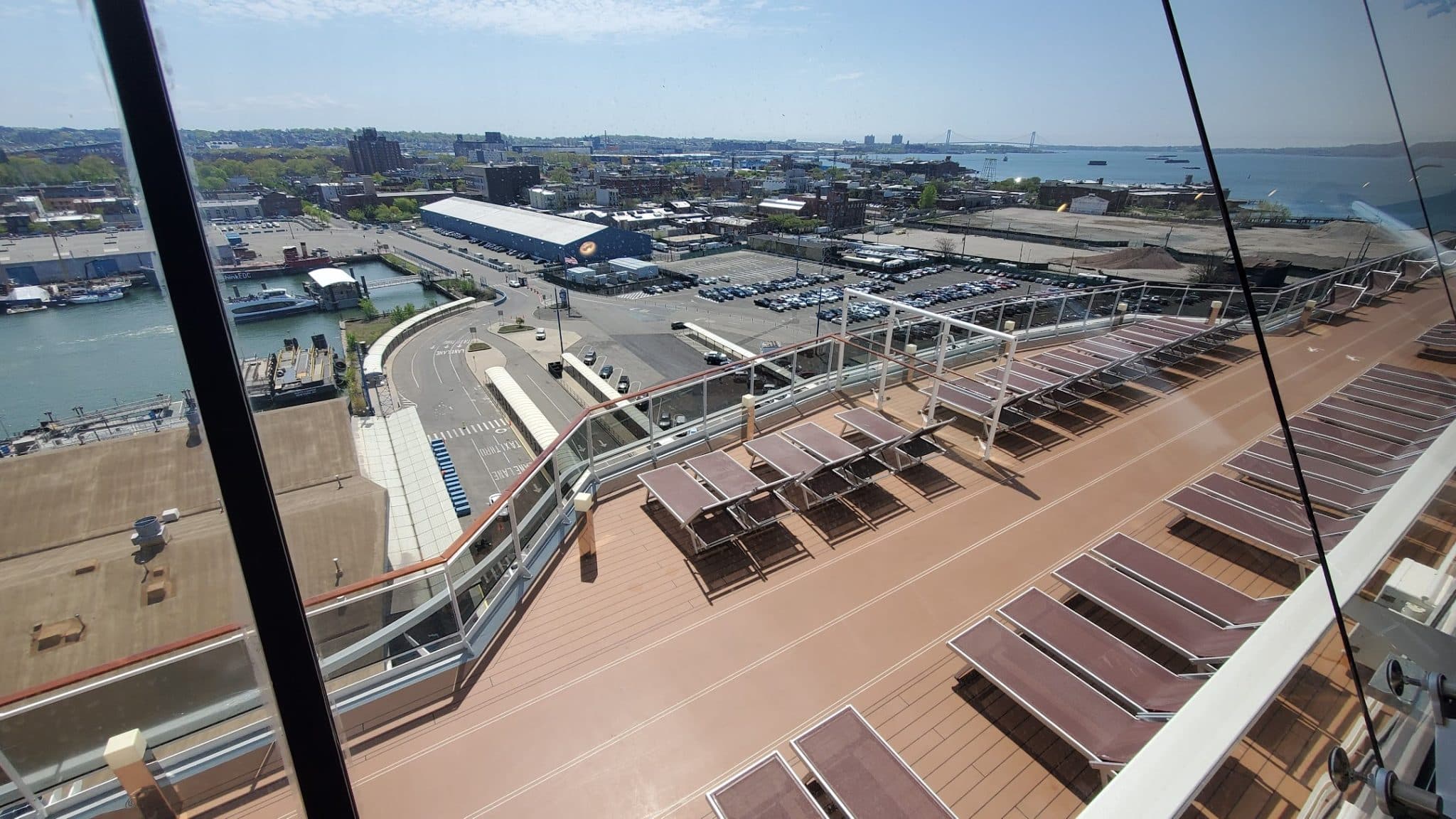 Sun deck of a docked cruise ship overlooking an industrial port and city under clear skies.