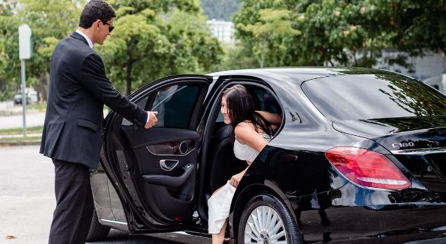 Bride stepping out of a sleek black Mercedes C180 limousine with chauffeur assistance, representing luxury wedding service.