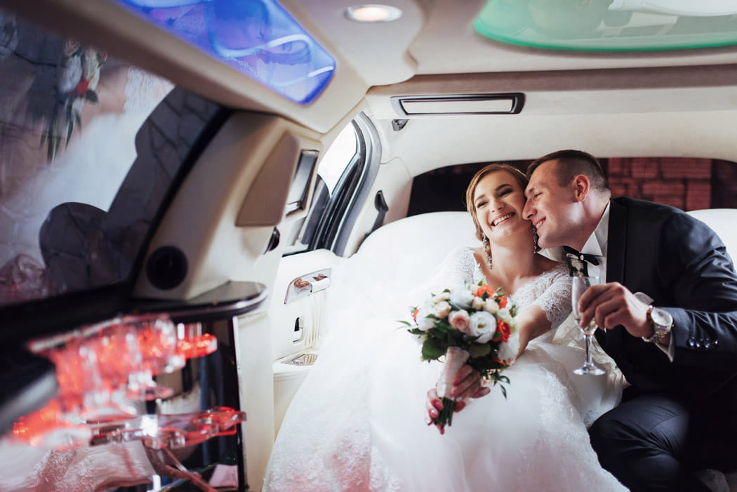 Bride and groom smiling and toasting with champagne inside a luxury limo, showcasing wedding service in New York.
