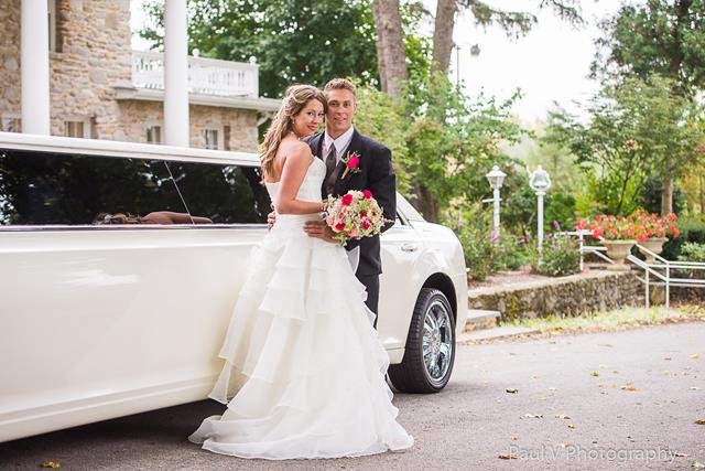 Bride and groom posing elegantly beside a luxurious white limousine, surrounded by beautiful garden scenery.