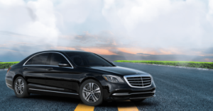 Luxury black Mercedes-Benz sedan parked on an open road with a scenic sunset and clouds in the background.
