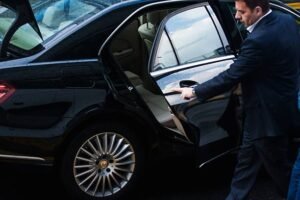 Chauffeur opening the rear door of a black luxury car for a passenger