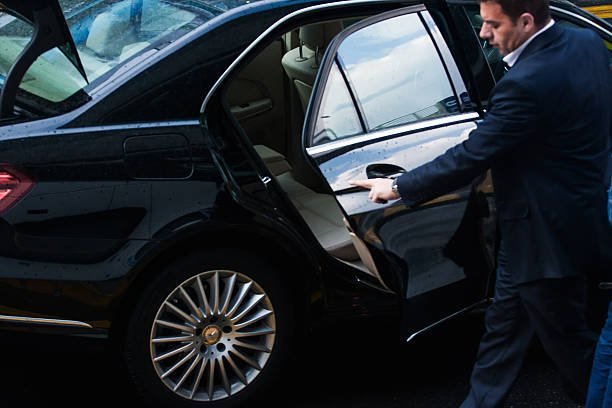 Chauffeur opening the rear door of a black luxury car for a passenger